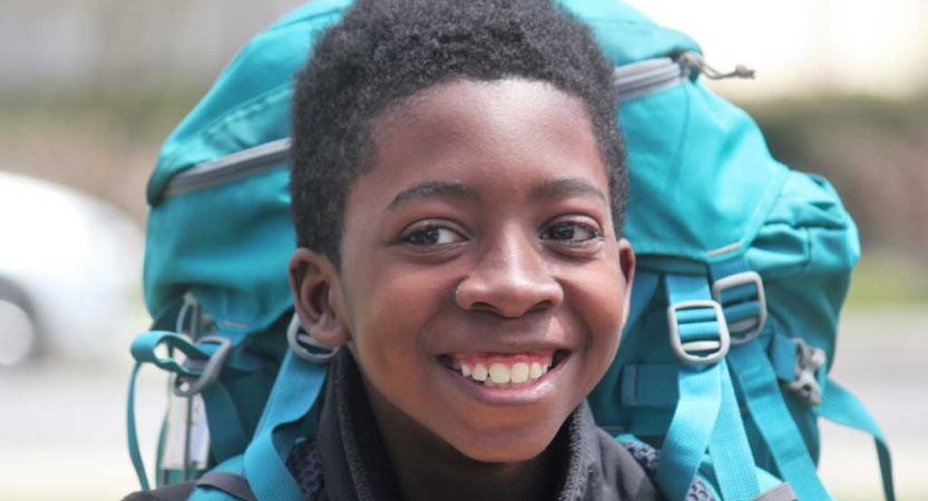 A young person wearing a backpack smiles at the camera 